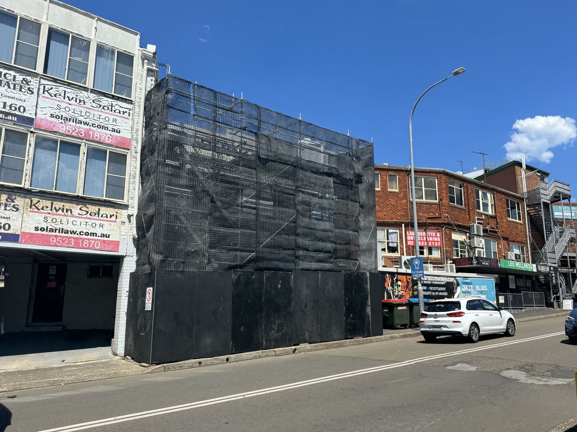 A white car is parked on the side of the road in front of a building under construction.