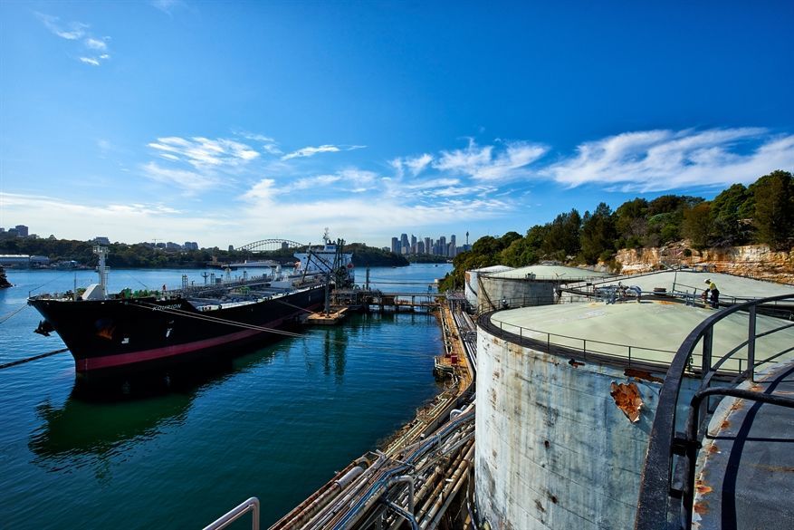 A large ship is docked in a harbor next to a large tank.