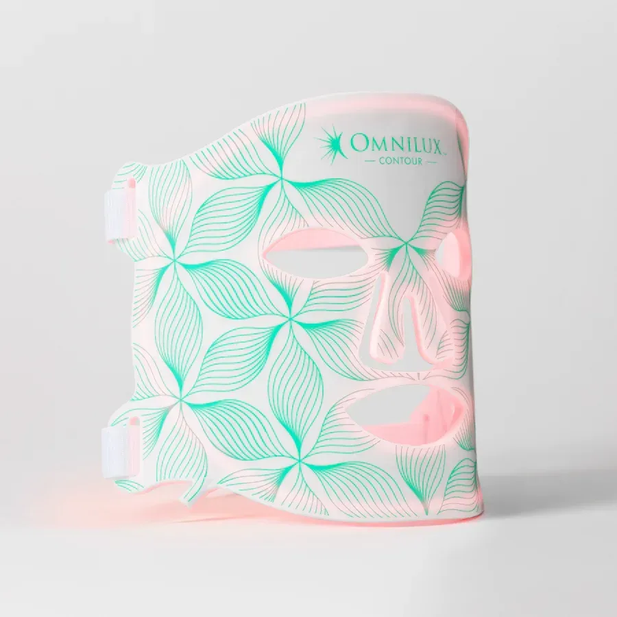 A pink and green mask with leaves on it is sitting on a white surface.