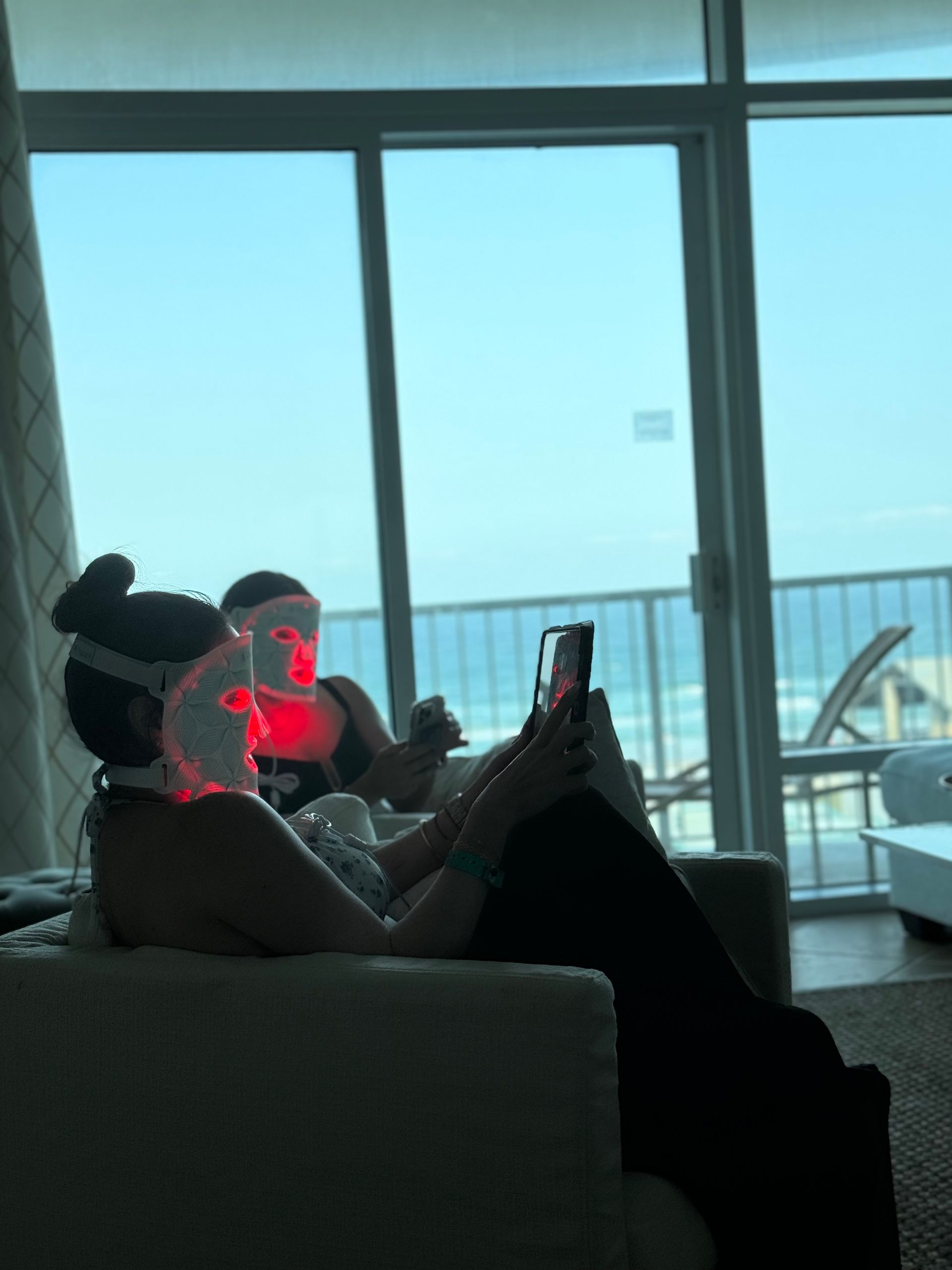 A woman is relaxing beach side with an LED mask on her face