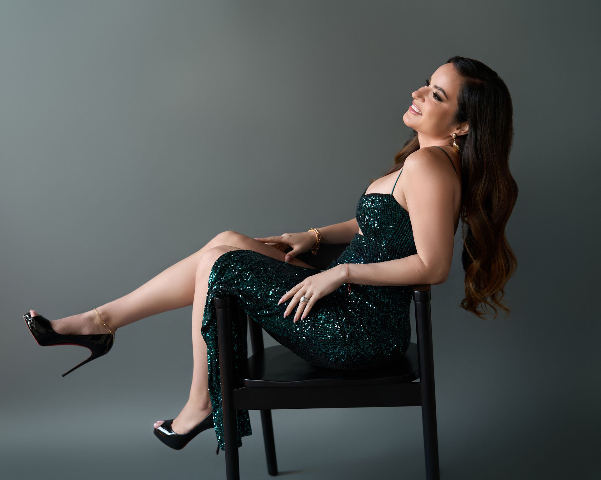 A woman in a green dress is sitting on a chair with her legs crossed.