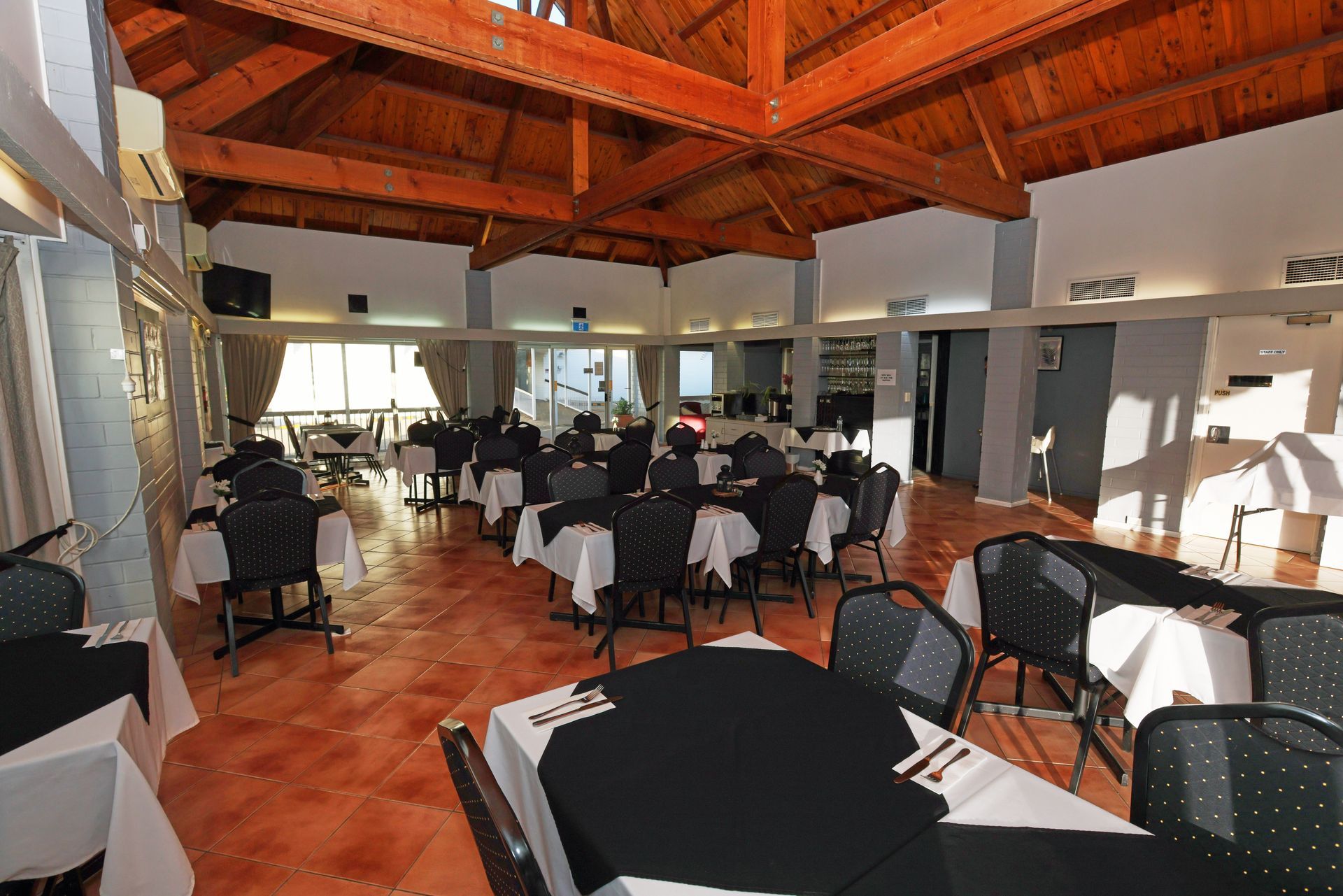 Indoor restaurant dining room with black chairs, white tablecloths, and a wooden vaulted ceiling