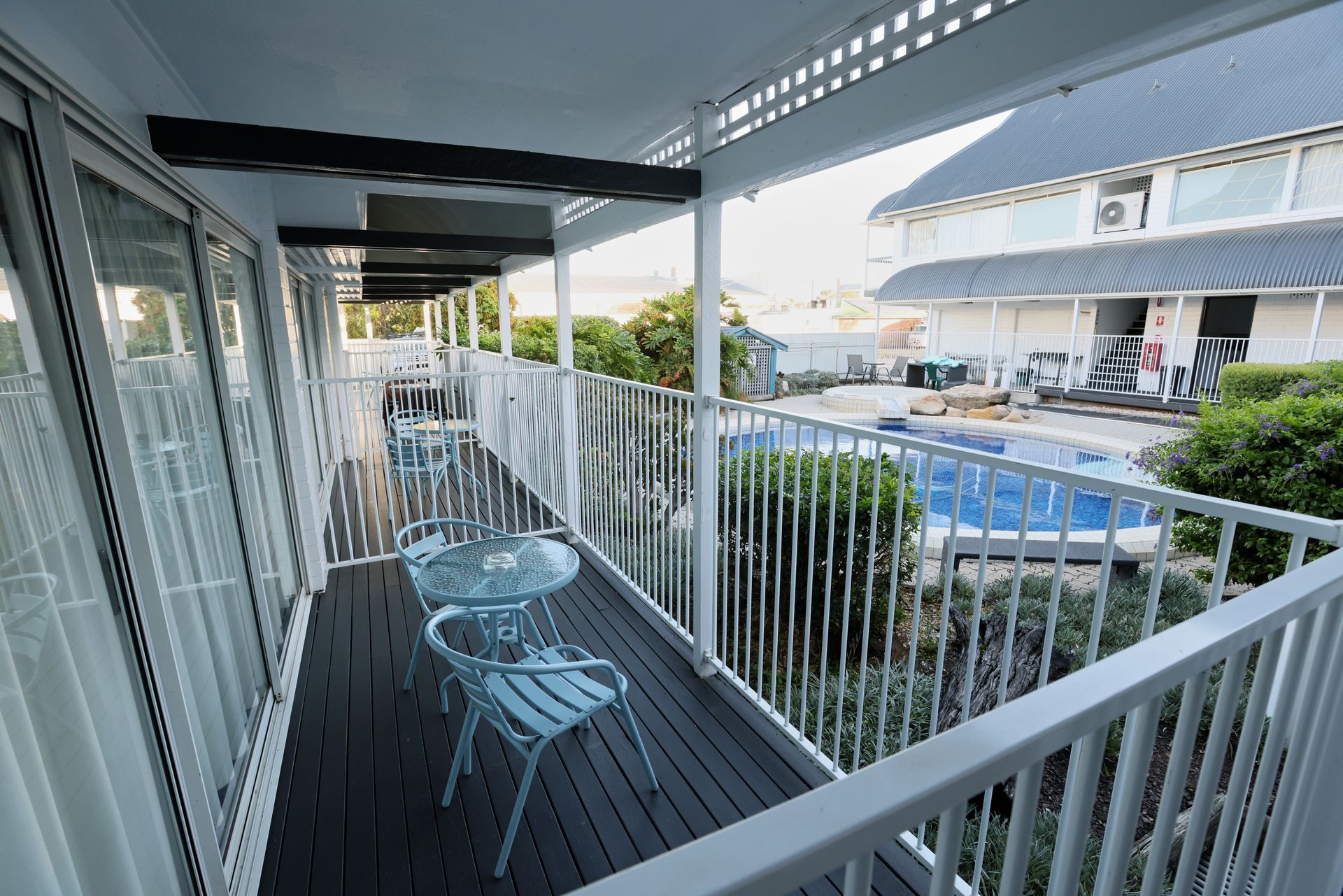 Balcony with white railing, blue chairs and table overlooking a pool and neighboring buildings