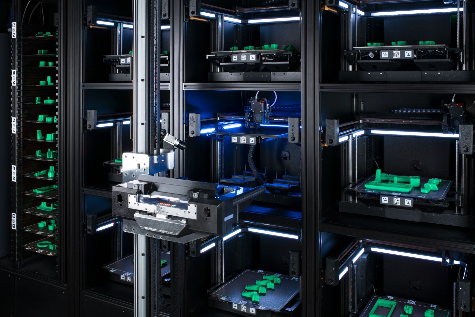 Automated 3D printing farm with several black enclosed units, each with a 3D printer and printed green parts.