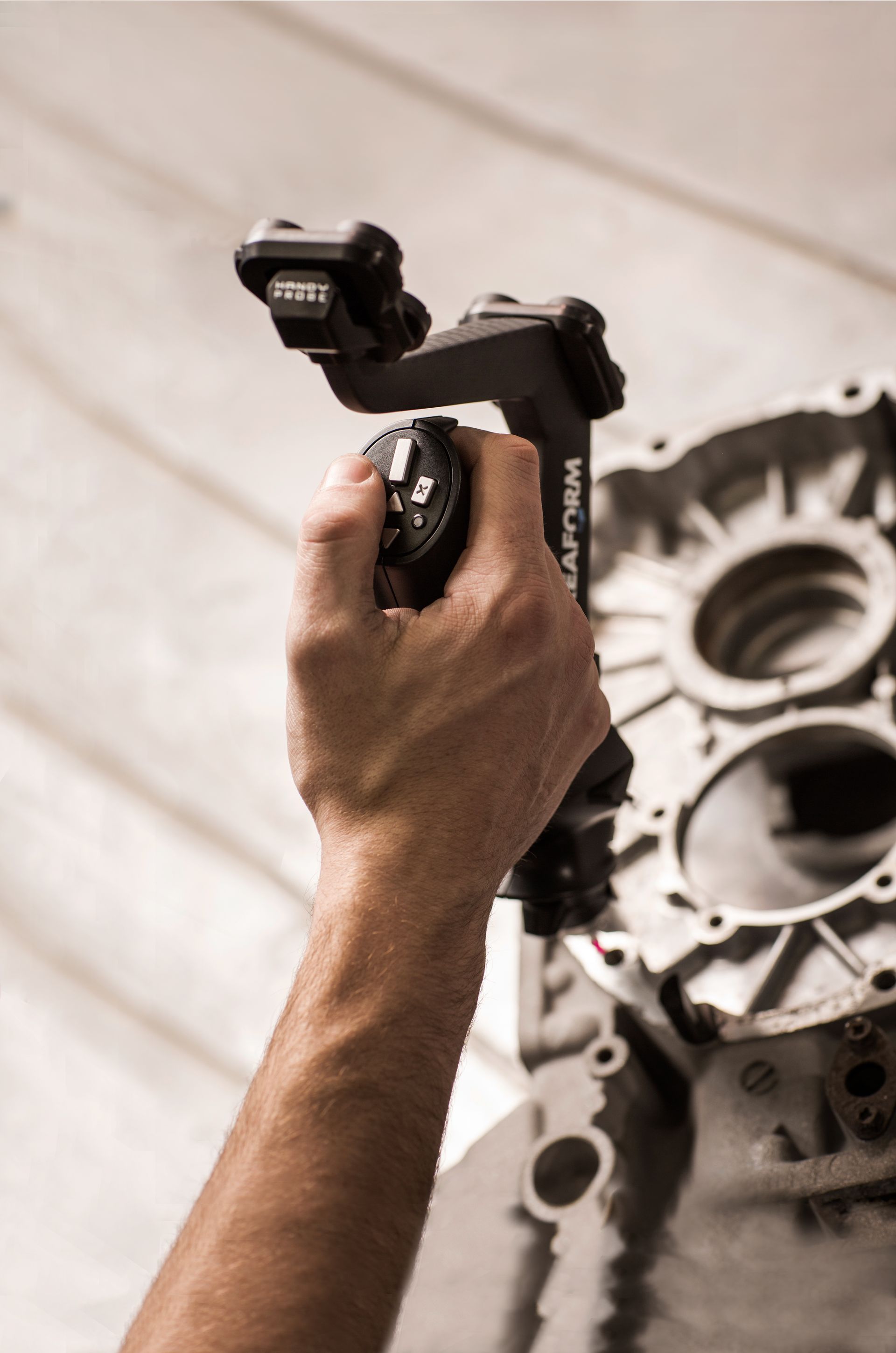 A person is holding a tool in their hand in front of a piece of metal.