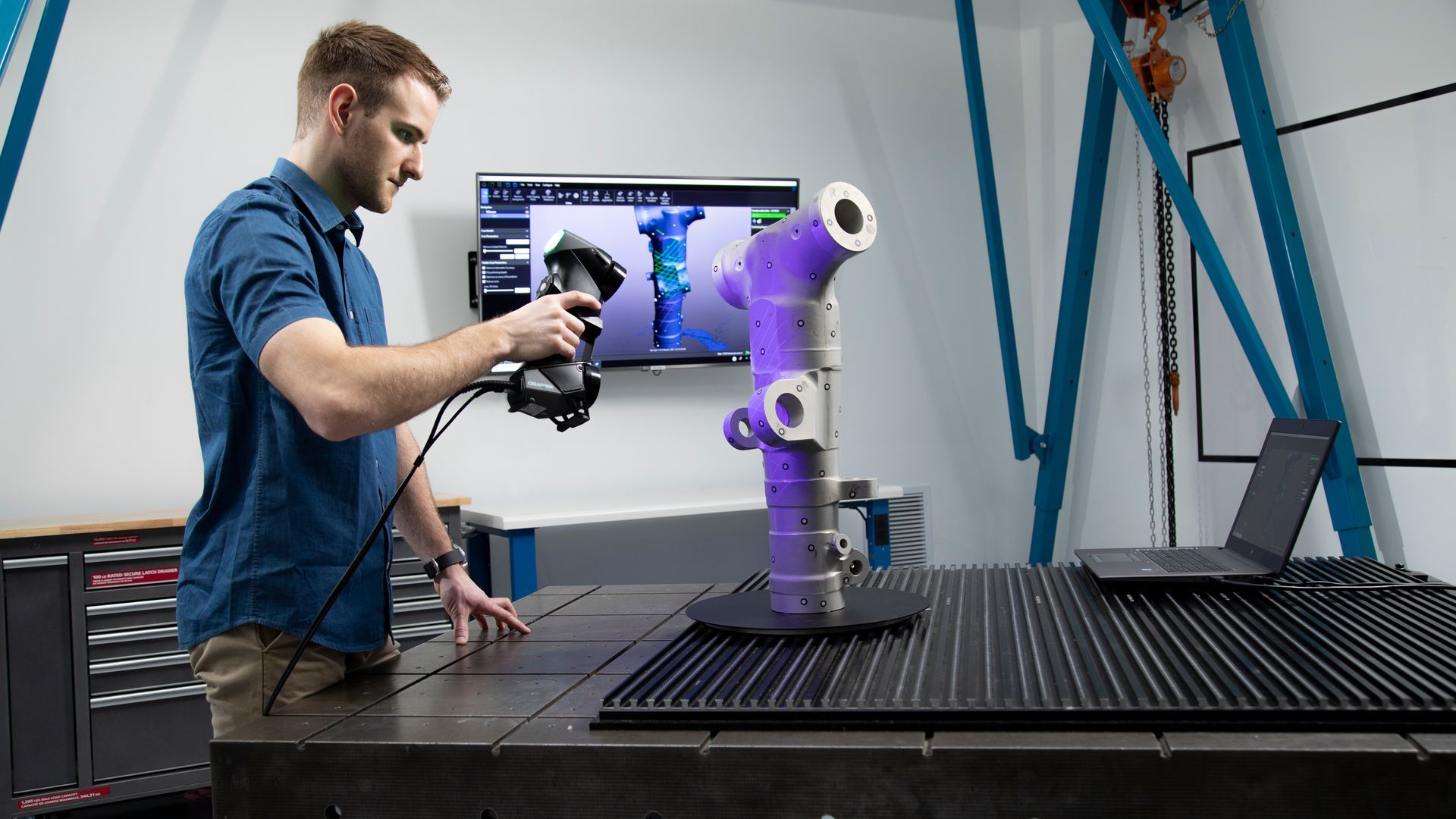 A man is using a 3d scanner to scan a pipe on a table.