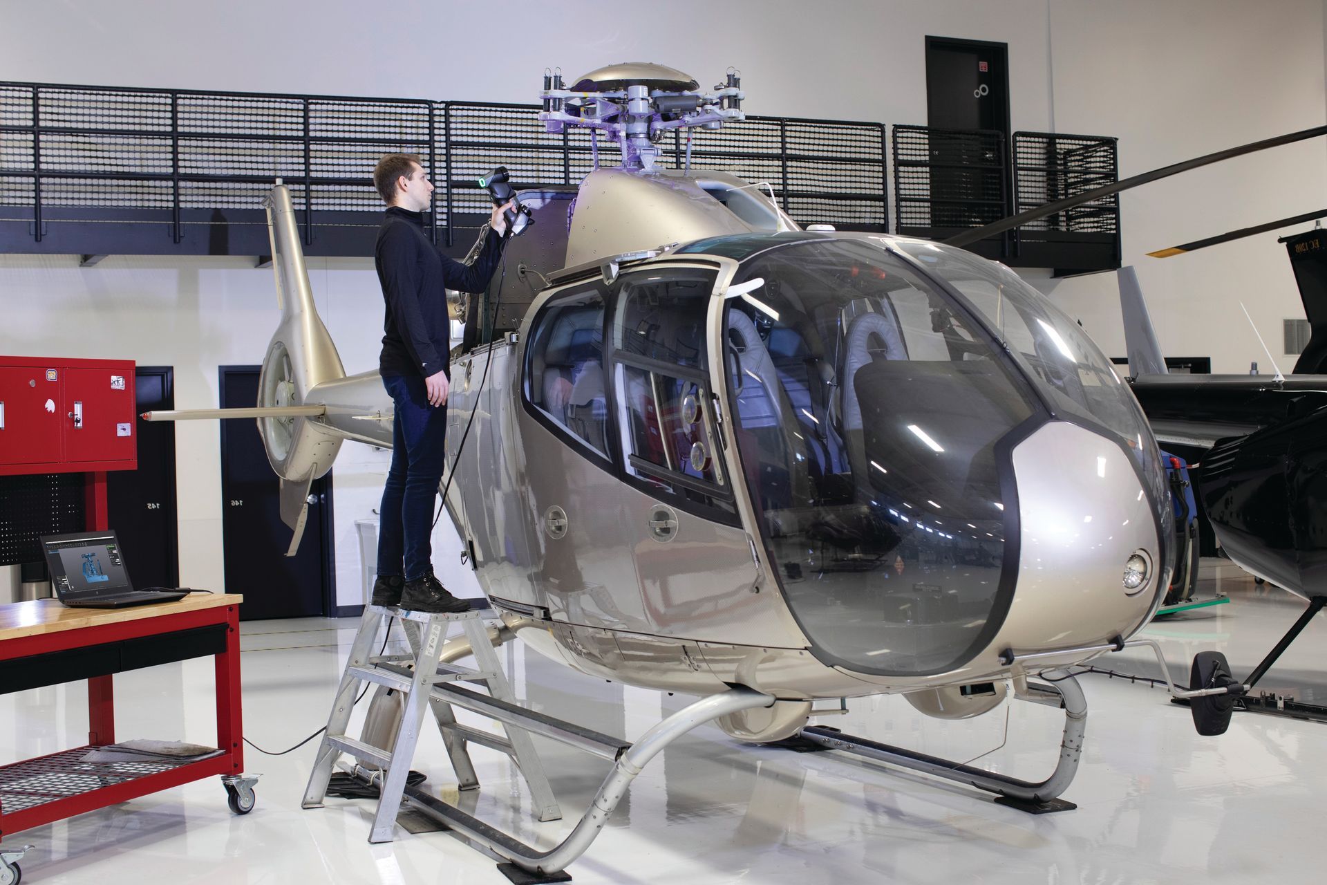A man is standing on a ladder next to a helicopter in a hangar.