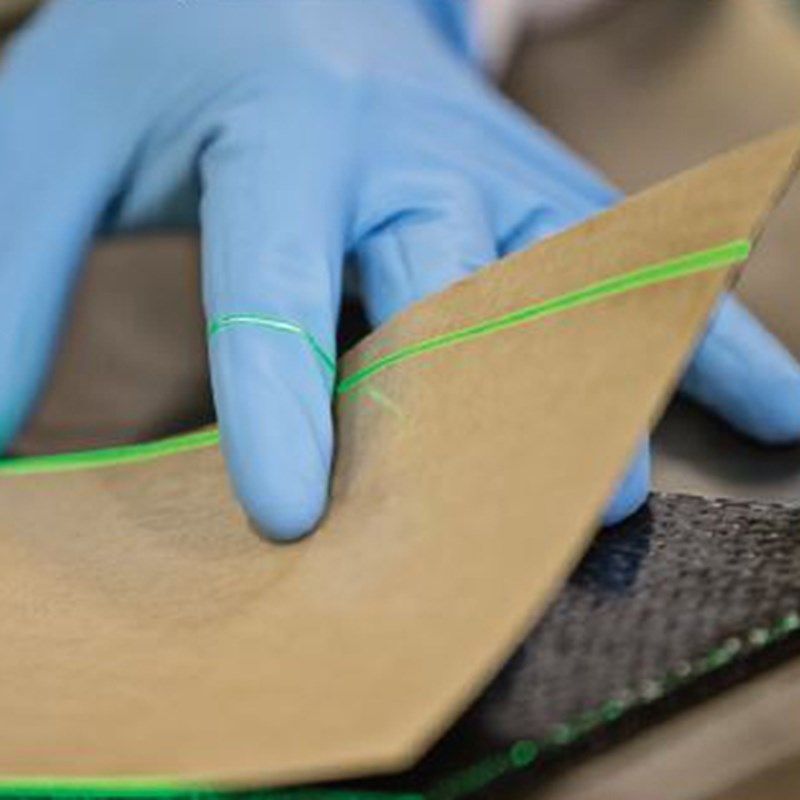 Gloved hand holding a brown, curved sheet with a green laser line, over a dark surface.