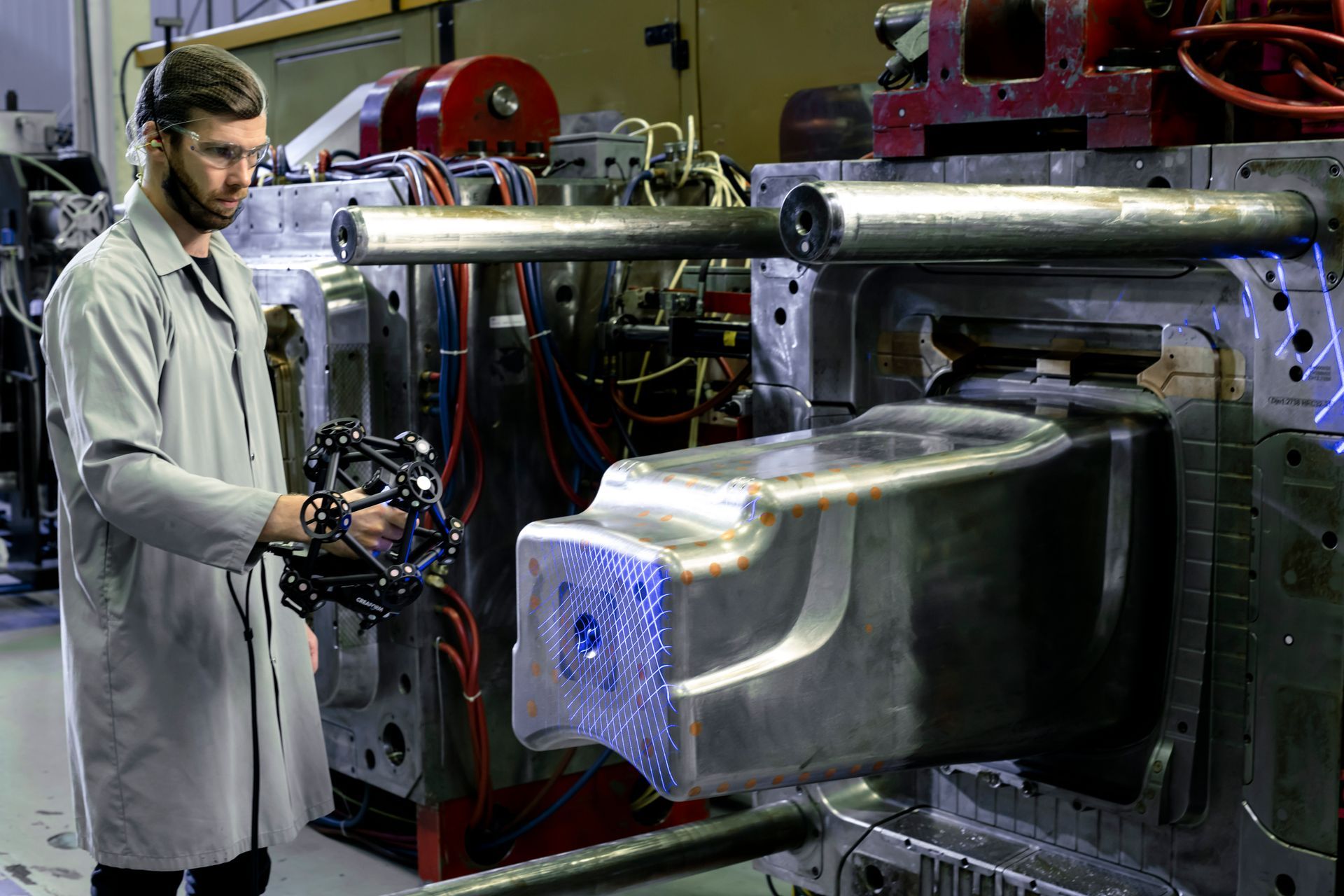 A man is standing in front of a machine in a factory holding a 3d model.