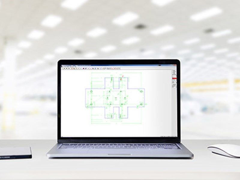 Laptop displaying a green and blue technical drawing, on a white desk with mouse and drive, bright background.