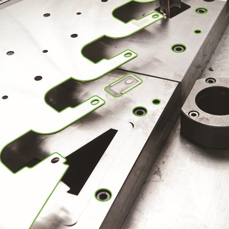 Metal industrial die with green highlighted cutouts and circular holes.