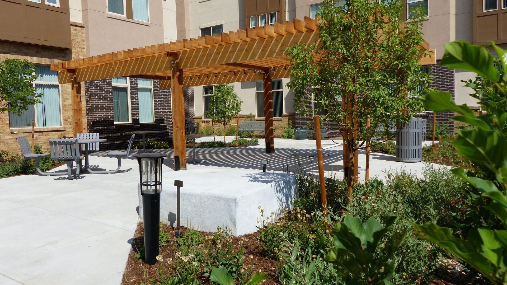 Courtyard patio with wooden pergola, white seating, potted plants, and a building backdrop