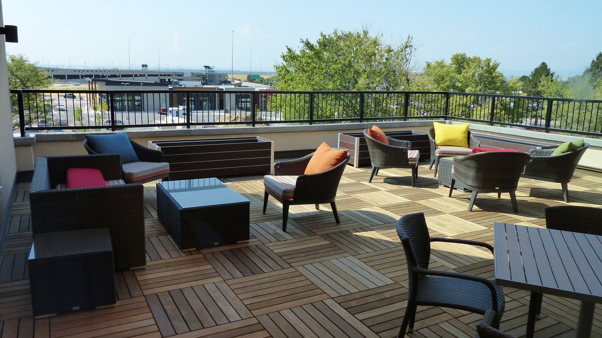 Outdoor rooftop patio with wicker seating, tables, and colorful cushions overlooking a city skyline