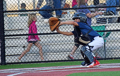 Baseball glove with ball on green grass, with blurred baseballs in the background.