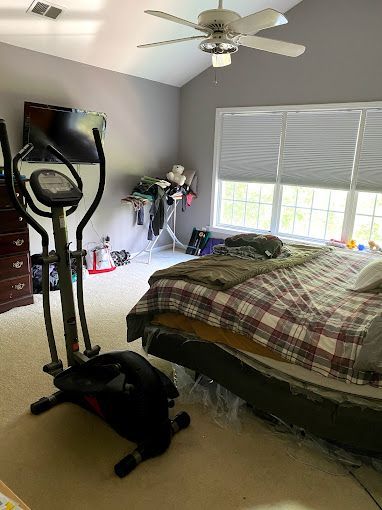 An elliptical machine is sitting in a bedroom next to a bed.
