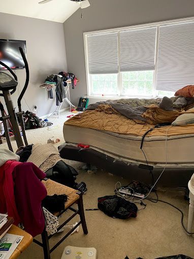 A messy bedroom with a bed , chair , exercise bike and television.