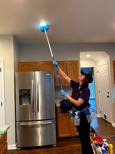 A woman is cleaning the ceiling of a kitchen with a mop.