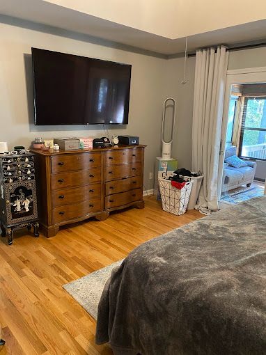 A bedroom with a bed , dresser , television and sliding glass door.