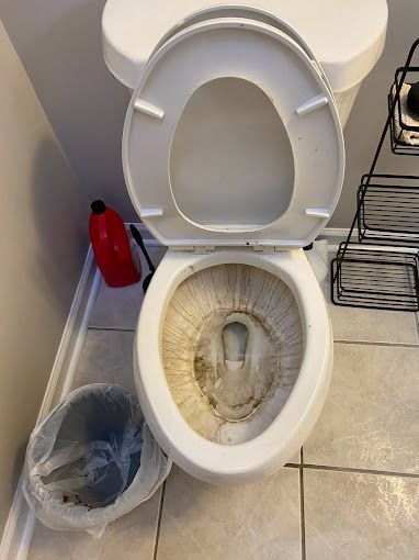A dirty toilet is sitting on a tiled floor next to a trash can.
