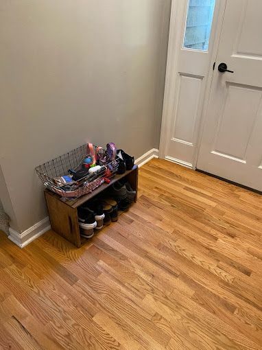 A wooden shoe rack filled with shoes is in a hallway next to a door.