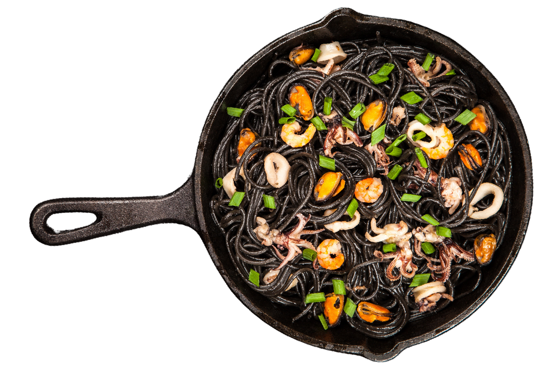 Una padella piena di tagliatelle e frutti di mare su sfondo bianco.