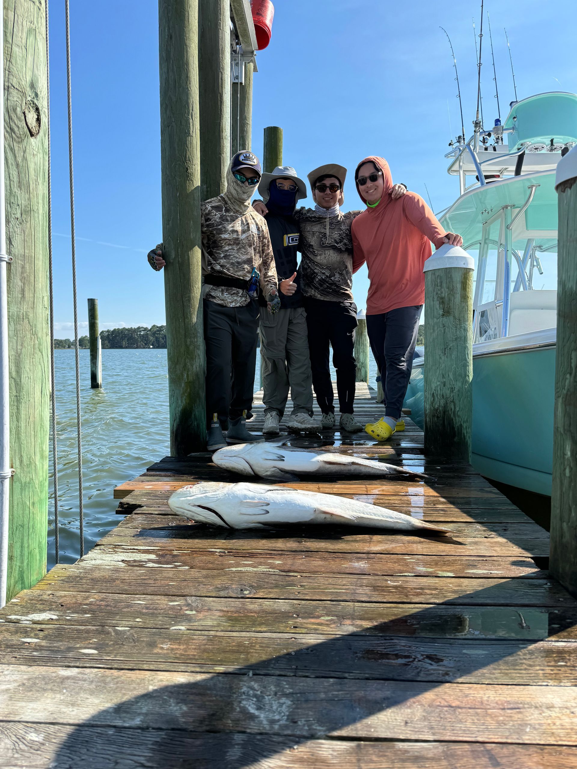 A group of people are standing on a dock holding fish.