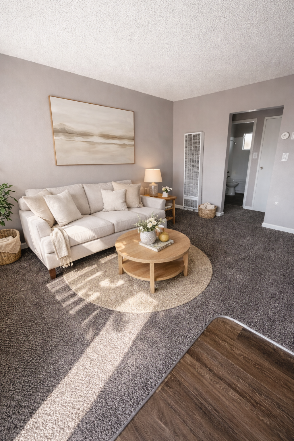 Cozy living room with cream sofa, round coffee table, beige wall art, and gray carpet.