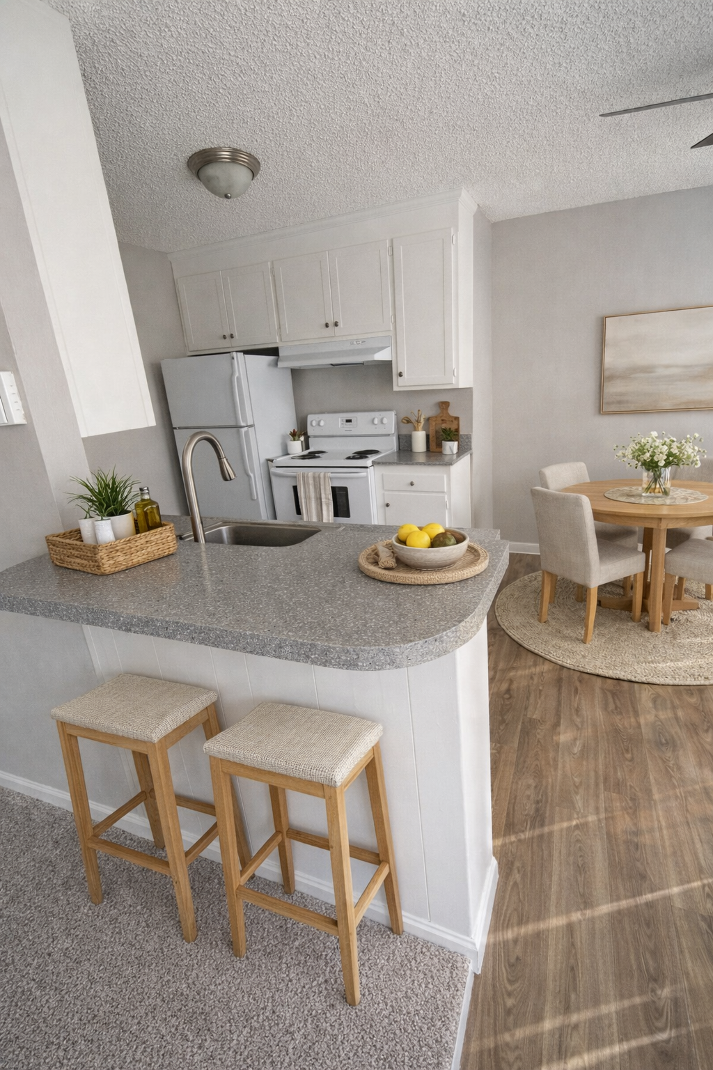 Bright modern kitchen with gray counters, white cabinets, stools, and a small dining table