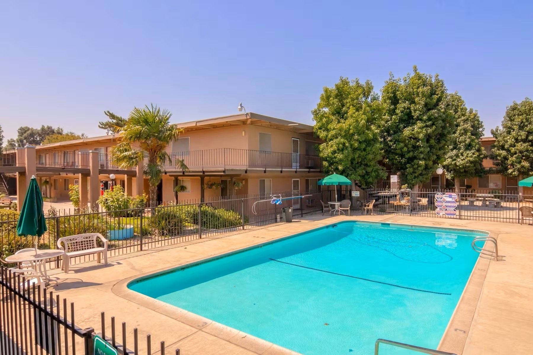 Sunny outdoor swimming pool beside tan apartment buildings and trees