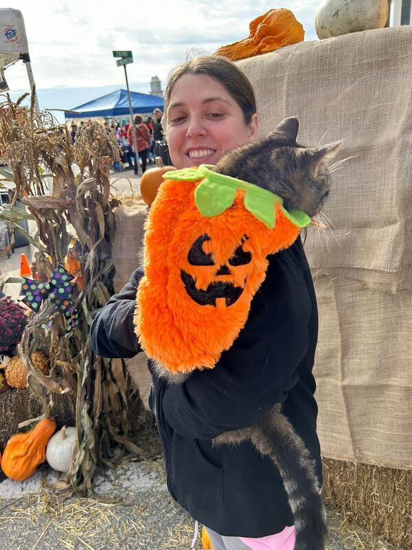 A woman is holding a cat wearing a pumpkin costume
