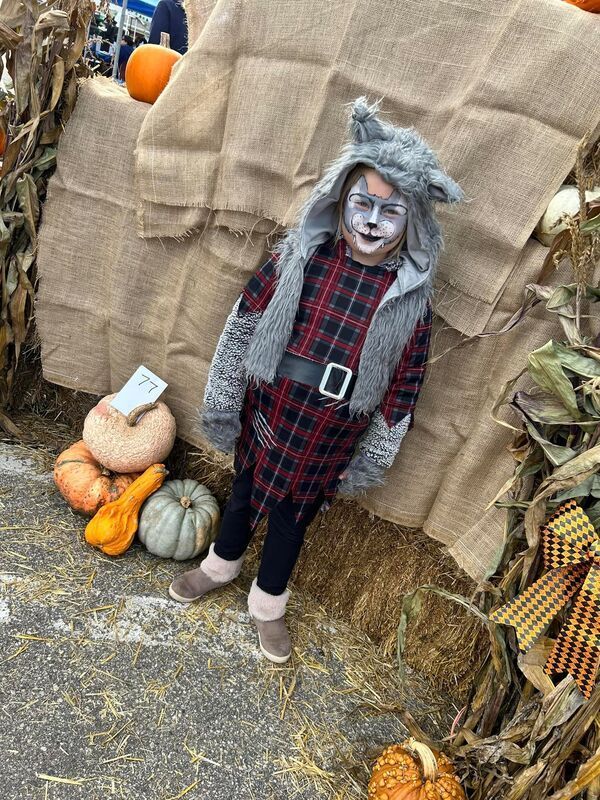 A little girl in a wolf costume is standing in a pumpkin patch.