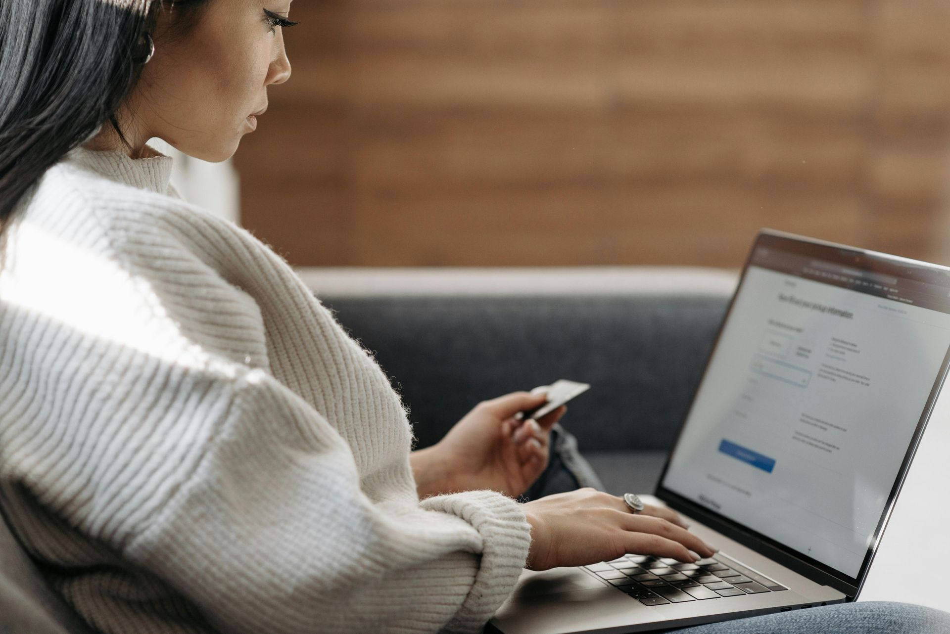 A woman is sitting on a couch using a laptop computer while holding a credit card.