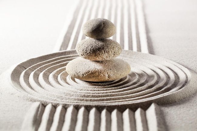 Three rocks are stacked on top of each other on a sandy surface.
