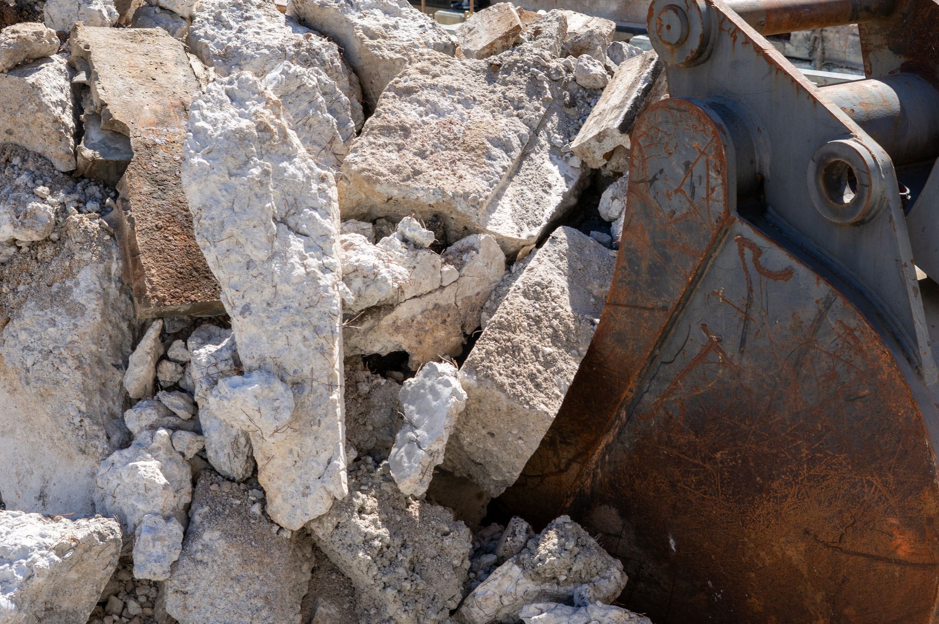Metal excavator bucket with large concrete blocks during demolition work on a construction site
