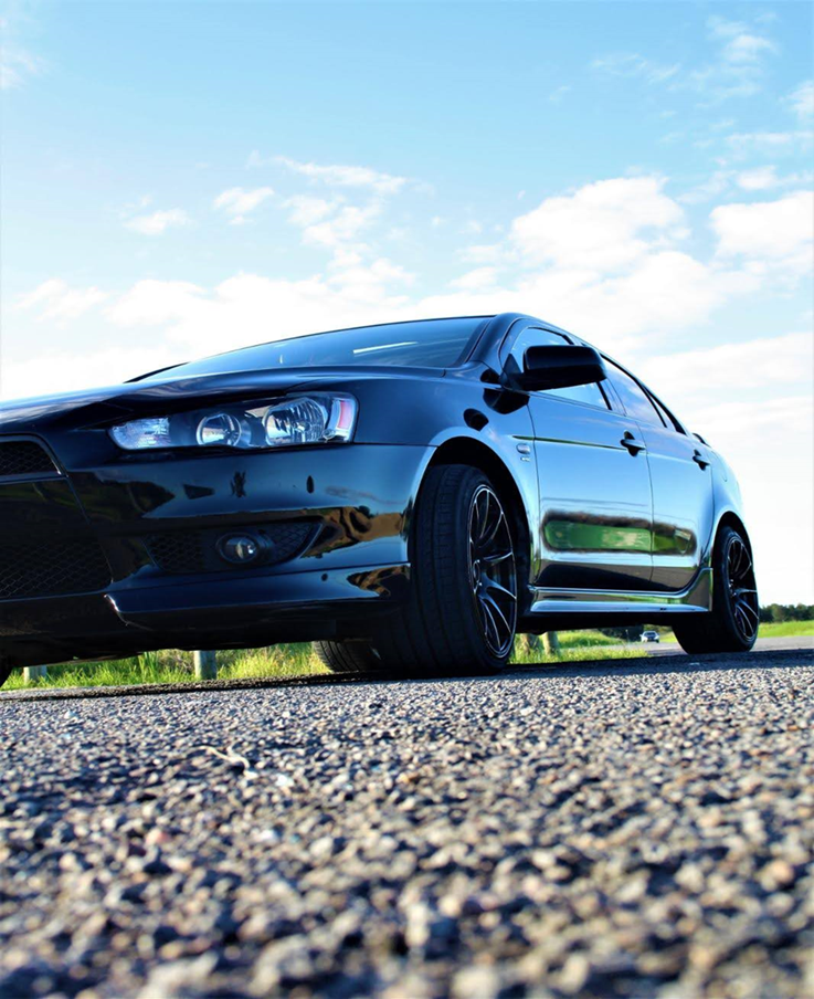 A black car is parked on the side of a gravel road.