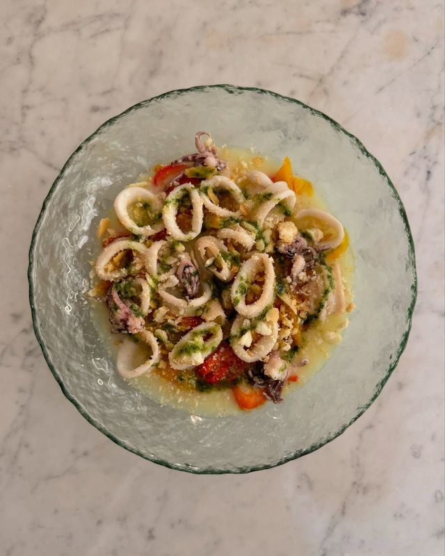 Una ciotola di cibo con calamari e pomodori su un tavolo.