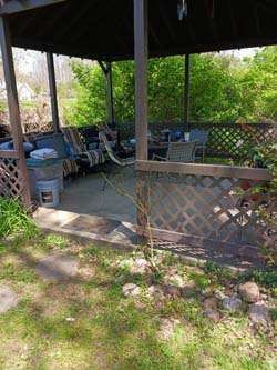 Covered outdoor patio with lattice railing, chairs, and a table in a grassy yard.