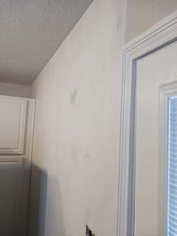 White hallway wall beside a doorframe and kitchen cabinet, with a small mark near the center.