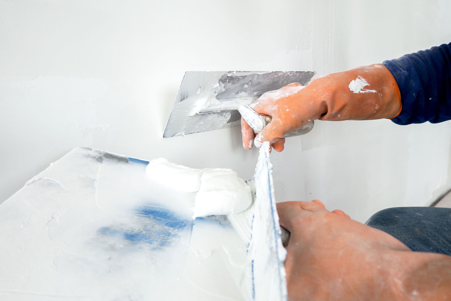 Person using a putty knife to apply white plaster to a wall during repair work