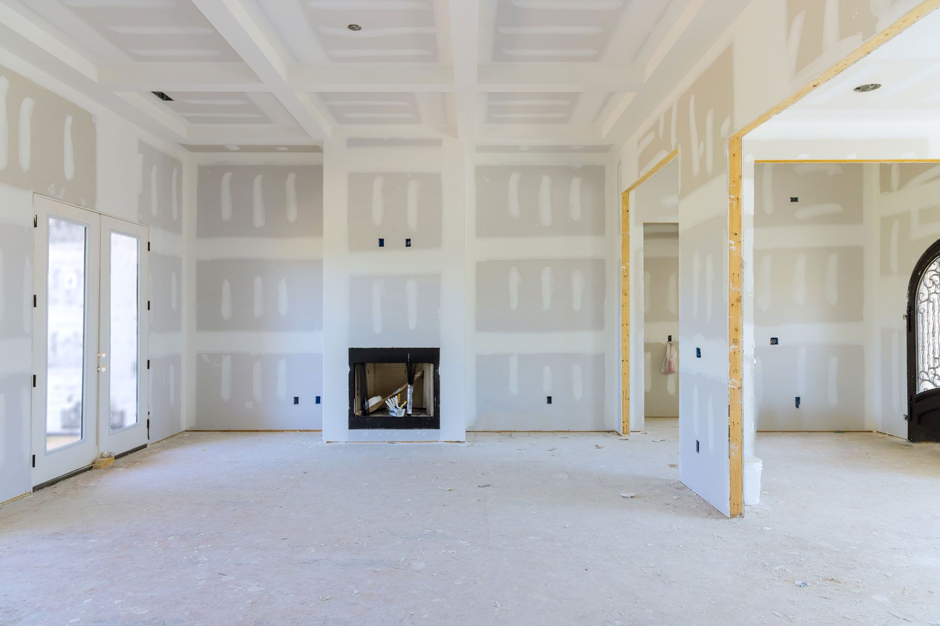 Unfinished white living room with a fireplace, high tray ceiling, and large windows/open doorway
