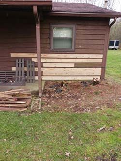 House exterior with repaired wood siding and a small window above a dirt and grass yard.
