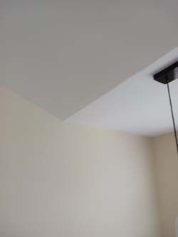 White ceiling corner with a dark rectangular ceiling fixture and a hanging cord against beige walls