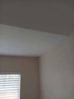 Empty beige bedroom corner with a window and closed blinds.