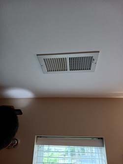 Ceiling air vent above a window with blinds in a beige room