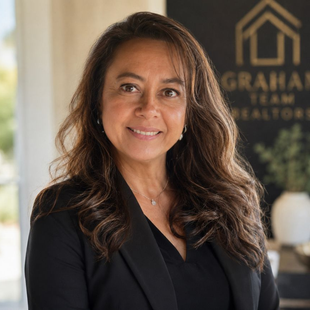 Portrait of a smiling woman in a black blazer standing before a blurred real estate office sign