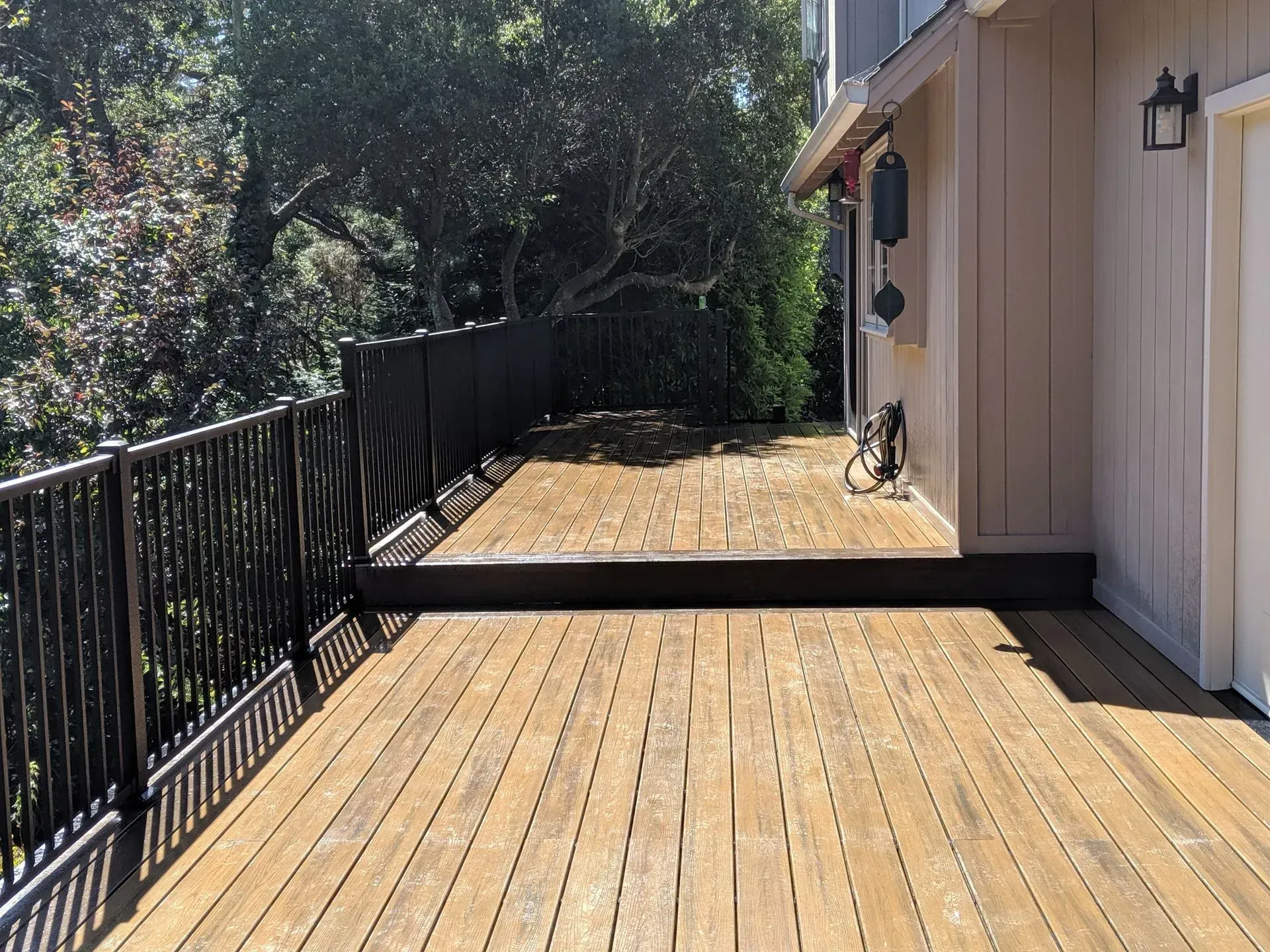 Wooden deck beside a house with black railing and trees in the background