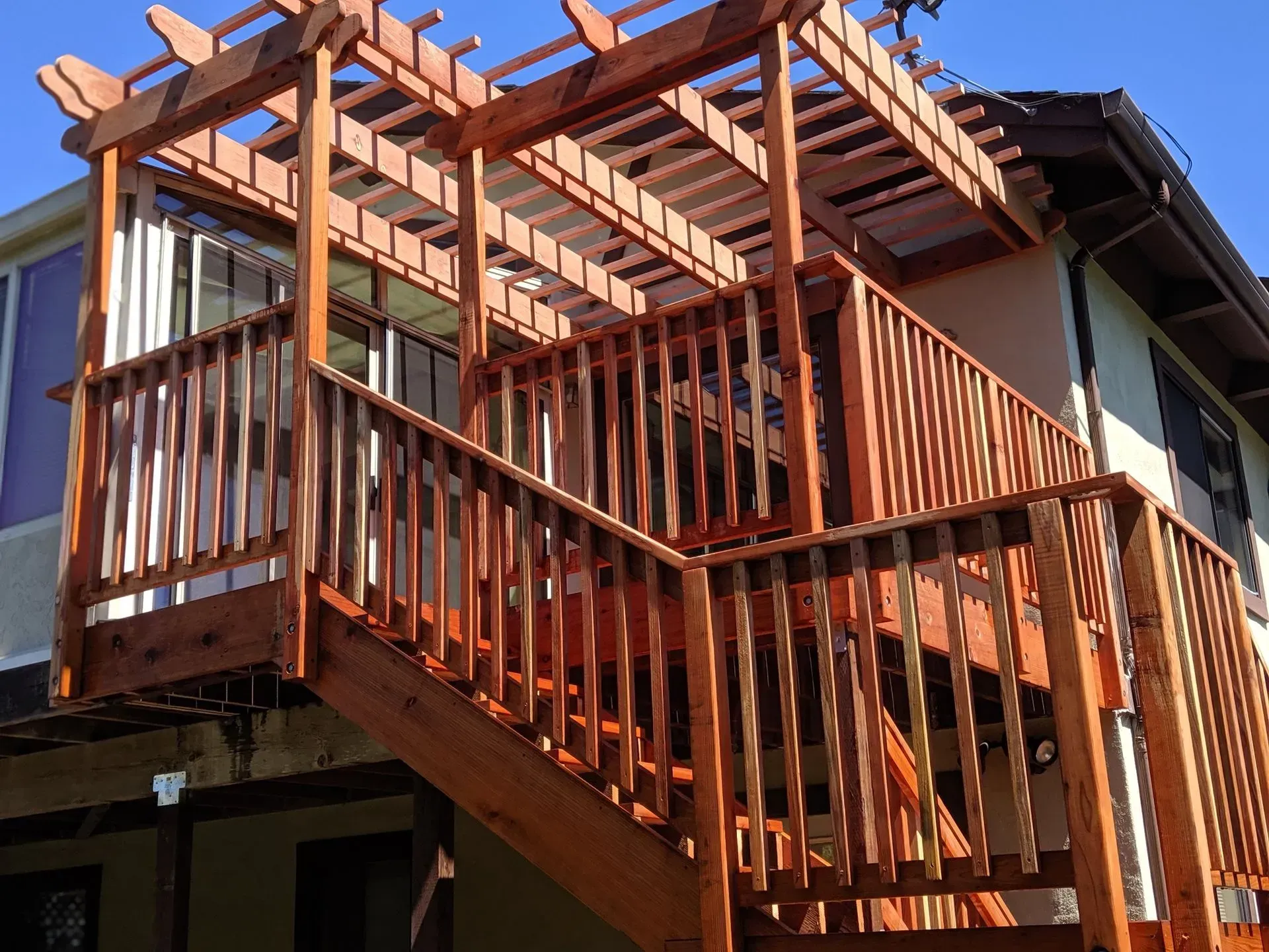 Exterior wooden staircase and balcony under construction on a house, with exposed beams and railings.