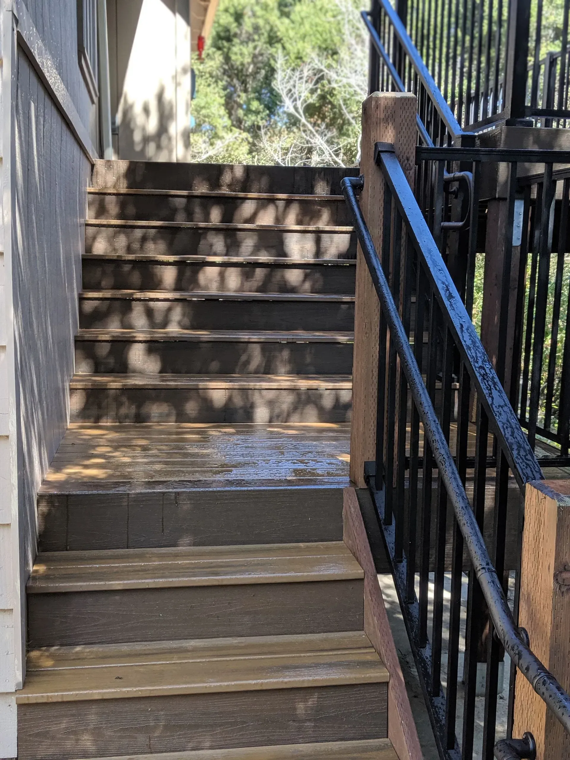 Outdoor concrete stairway with black metal railings and a blue handrail in sunlight