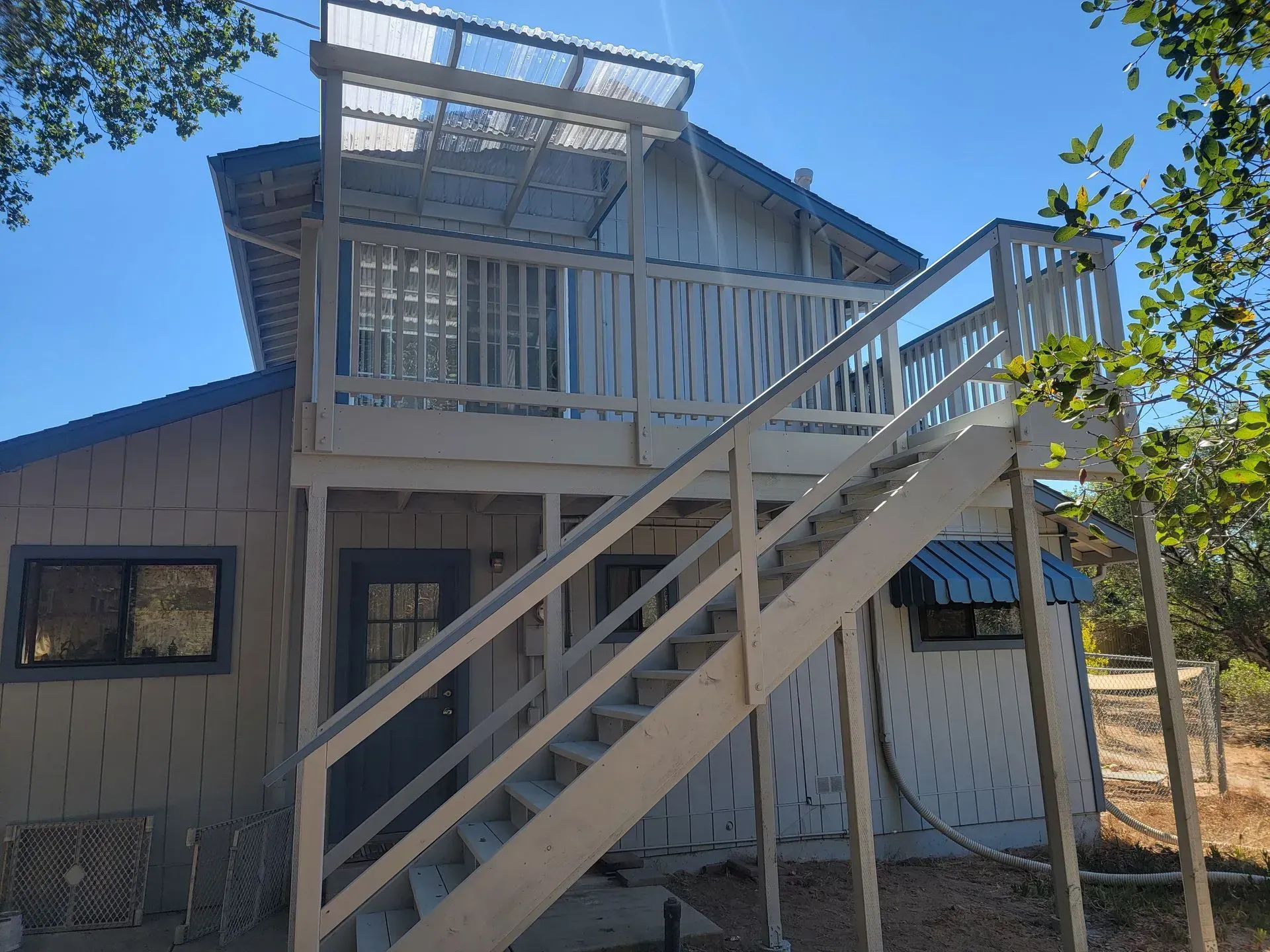 Two-story house with exterior staircase and white balcony railing under a bright blue sky