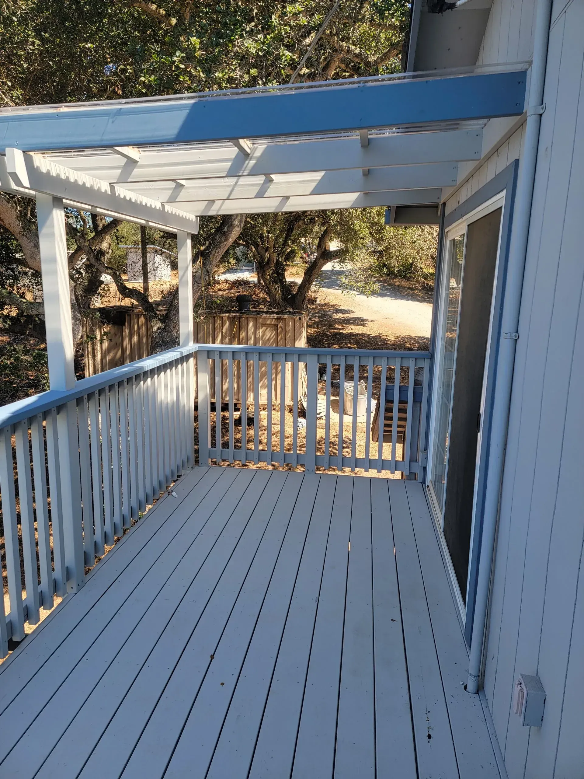 White wooden porch with railing and pergola, overlooking trees in daylight.